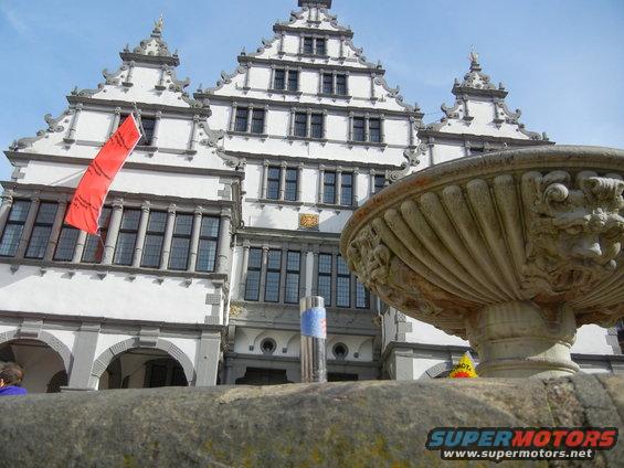 Stone fountain in front of a large, ornate building with a red banner