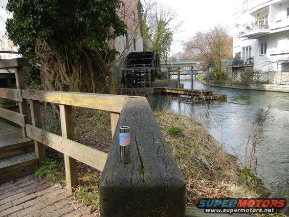 Wooden bridge railing in foreground, water wheel and canal in background