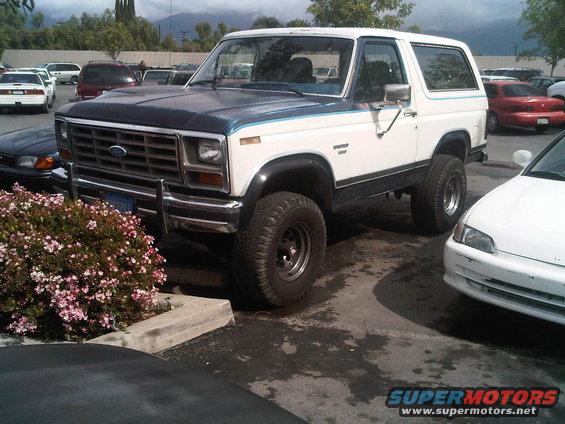 White and blue Ford Bronco with lifted suspension and off-road tires, parked in a lot