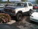 1986 Ford Bronco - A white and blue Ford Bronco is parked in a lot next to other vehicles.