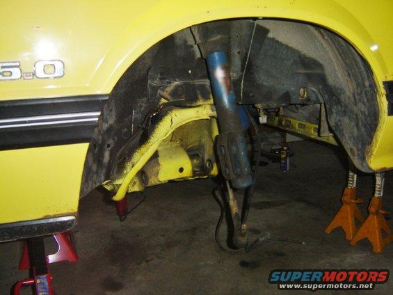 Yellow 1979 Ford Mustang front wheel well with 5.0 badge visible, car on jack stands