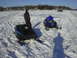 1987 Polaris Indy 600 - Two snowmobiles sit on a snowy landscape under a clear blue sky.