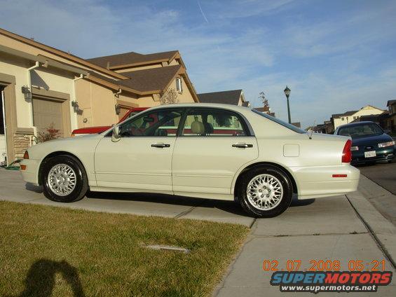 White sedan parked on a driveway, side view. The car has alloy wheels and a clean body