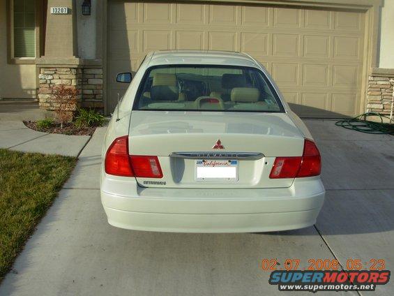 Rear view of a white sedan parked in front of a garage. Has a Mitsubishi badge and 'Diamante' text on the trunk