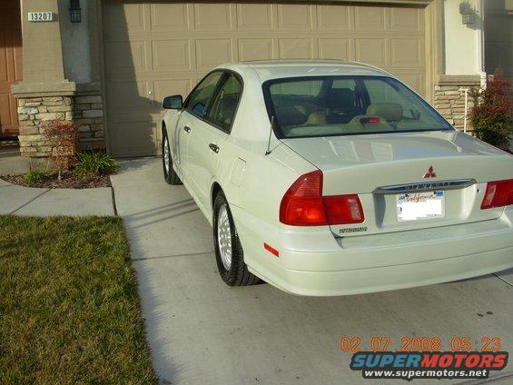 White sedan parked in driveway, rear 3/4 view. Visible badge on trunk