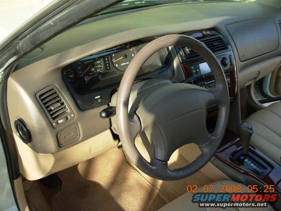 Car dashboard with steering wheel, beige dashboard, black steering wheel, tan floor mats