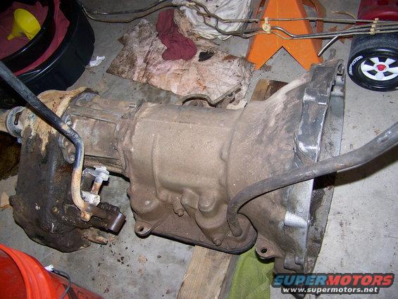 transmission assembly on floor, with oil pan, lines, and a yellow funnel nearby
