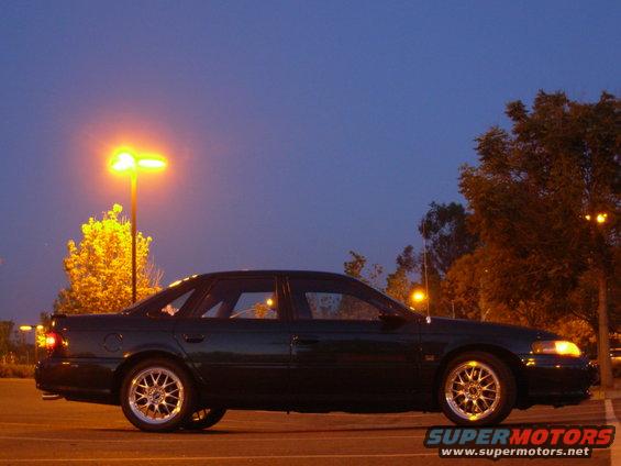 1995 Ford Taurus side profile at dusk, parked in a lot with streetlights