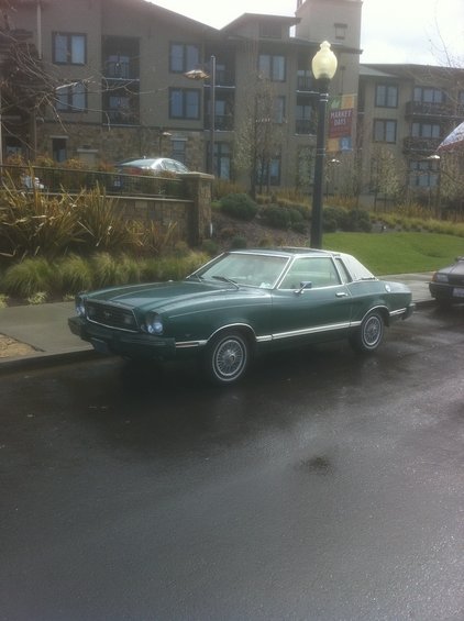 Green coupe with vinyl roof, side view. Appears to be a 1975 Ford Mustang II