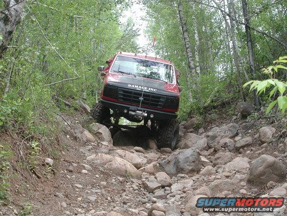Red truck with black hood and winch, navigating a rocky trail