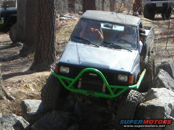 Gray Toyota pickup truck with a green brush guard navigating large rocks off-road