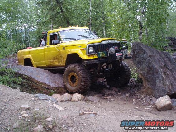 Yellow 1986 Jeep J-10 pickup truck with large tires navigating a rocky trail