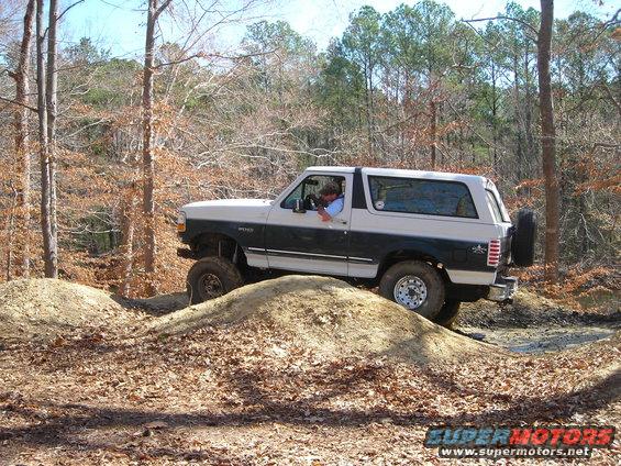 Two-tone 1995 Ford Bronco driving on dirt mounds off-road