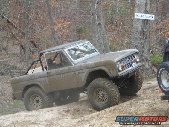 Mud-covered 1970 Ford Bronco with off-road tires on a dirt trail