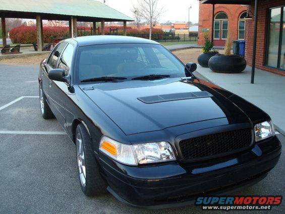 Black sedan with aftermarket grille and hood scoop, parked on asphalt