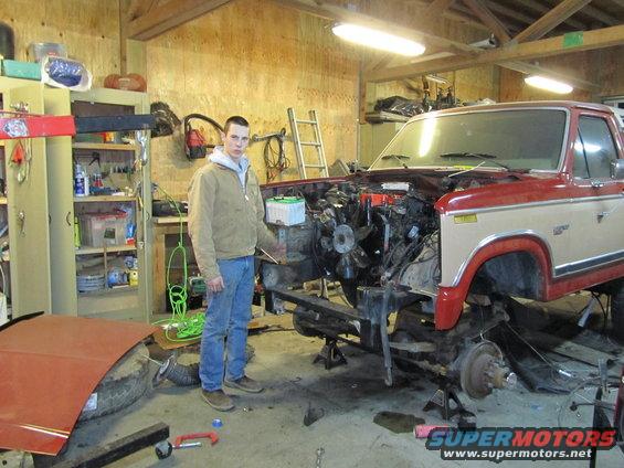 Red and tan Ford truck with engine removed, jacked up in a garage