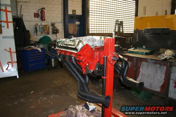 V8 engine on a stand, red block, chrome valve covers, black headers. Workshop background