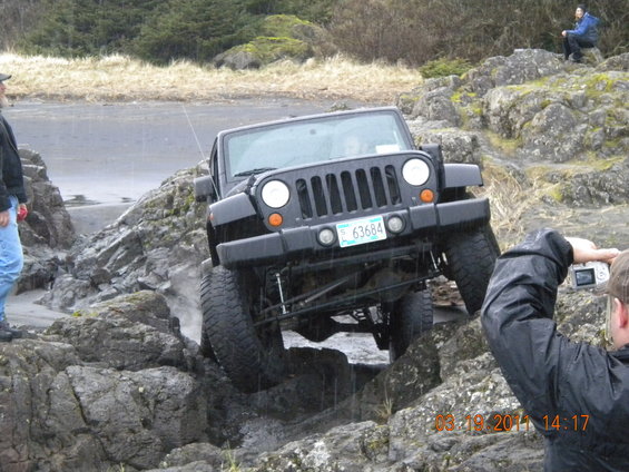 Black Jeep Wrangler navigating rocky terrain, front grille and license plate visible