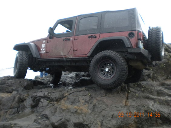 Red Jeep Wrangler on rocks, 3/4 front view