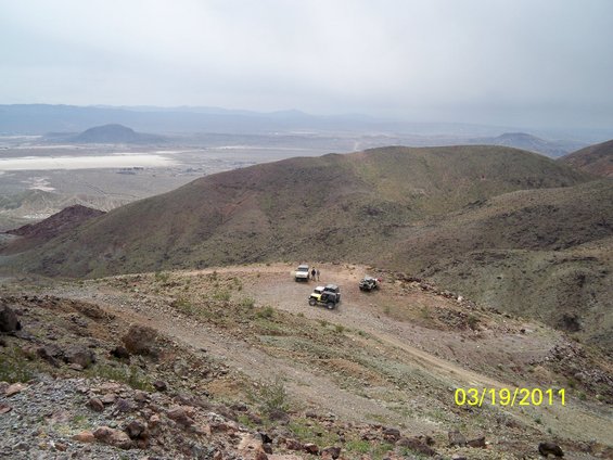 three off-road vehicles parked on a dirt path on a mountain overlooking a valley