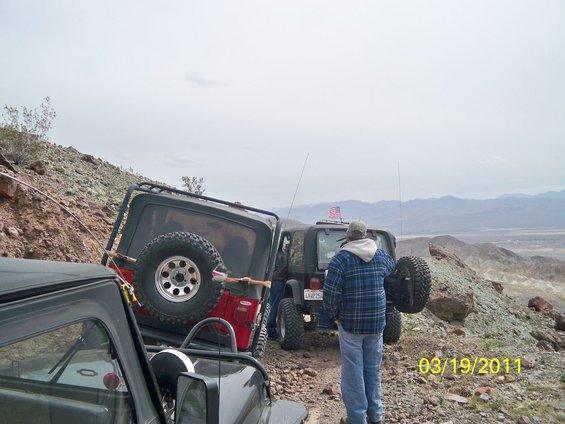 Two red and black Jeep Wranglers on a rocky hill, one tilted