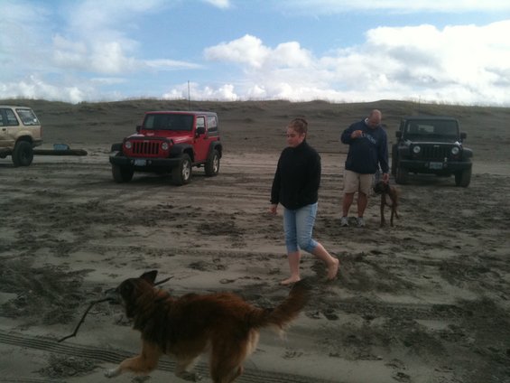Red Jeep Wrangler on sand, 3q-front view. Two other Jeeps visible