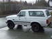 1996 Ford Bronco - A white Ford Bronco SUV is parked on a wet paved surface, viewed from the side.
