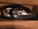2003 Ford Taurus - A single car headlight is shown, resting in a cardboard box. Text is visible on the headlight lens.