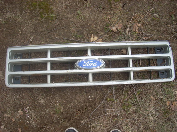 Silver Ford grille with blue oval emblem, horizontal bars, and black mounting clips