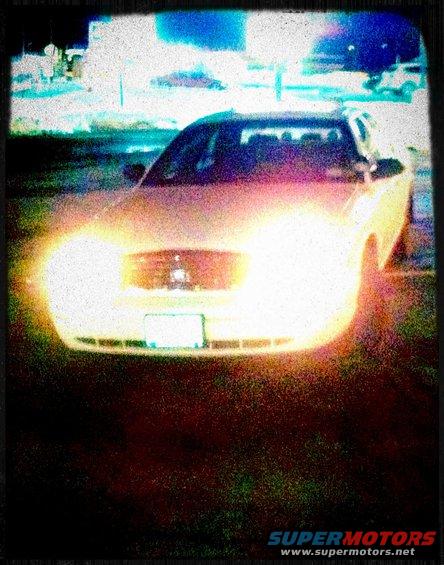 Front view of a sedan with headlights on, parked at night