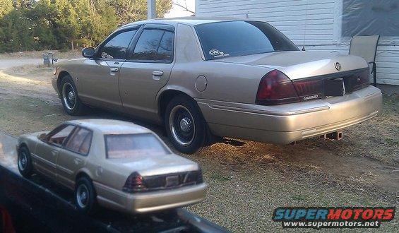 Tan sedan parked next to a toy tan sedan, rear 3/4 view