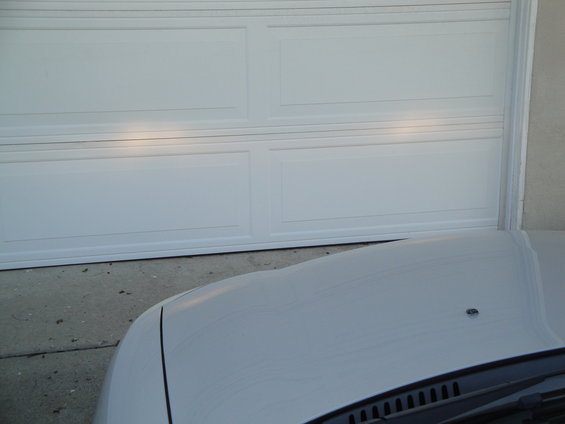 Car hood in front of white garage door. Headlights are on