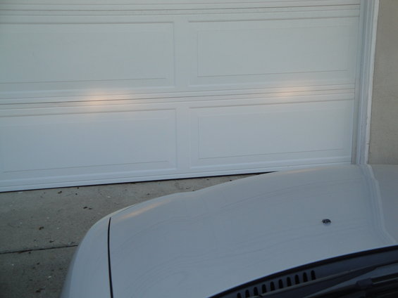 White car hood in foreground, white garage door in background with headlights on