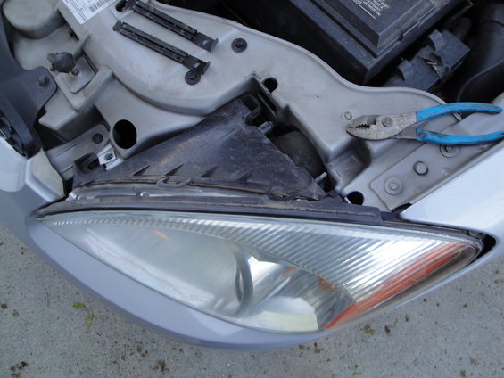 Car headlight assembly with pliers resting on the engine bay. Looks like a 2003 Ford Taurus