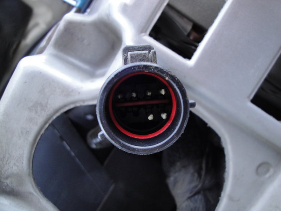 Close-up of a vehicle's headlight electrical connector with red and black housing and multiple pins