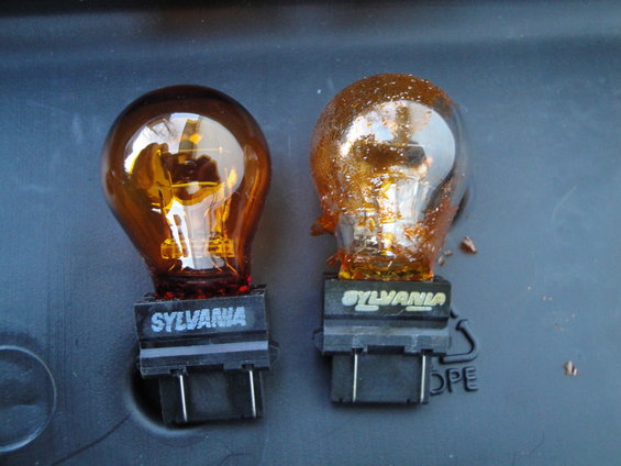Two Sylvania amber light bulbs, one looks new, the other is damaged and covered in debris