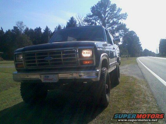Dark Ford Bronco parked on grassy shoulder next to a road, front view