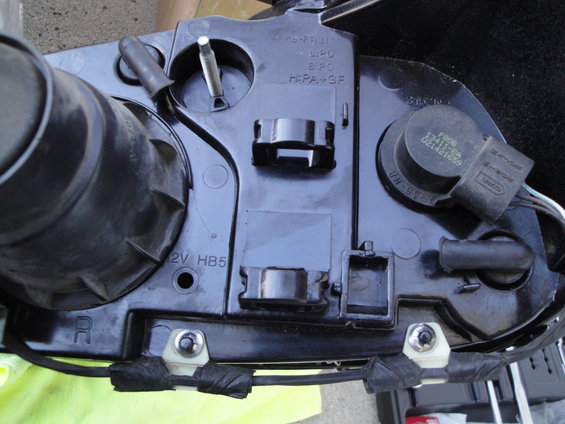 Back of a car headlight assembly with wiring and mounting hardware visible. Part number F809 13411-BA 021421699 is stamped on a component