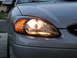 2003 Ford Taurus - The illuminated headlight of a silver 2003 Ford Taurus is shown from the front.