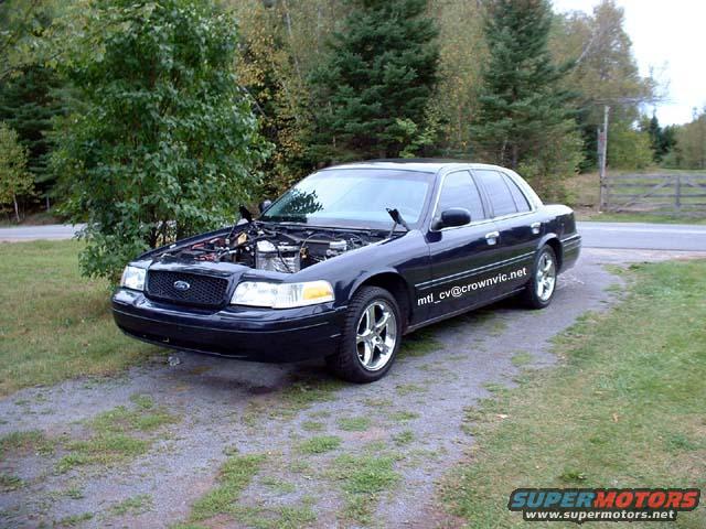 Dark blue 2000 Ford Crown Victoria with hood open, parked on a gravel driveway