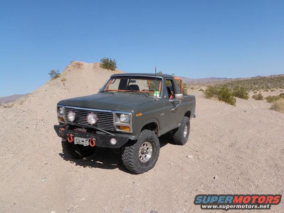 Green Ford Bronco with orange roll cage and aftermarket bumper parked on a dirt road