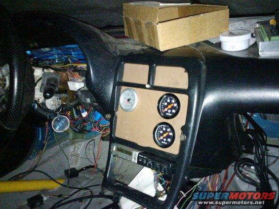 Car interior showing a mess of wires, a stereo, and three gauges installed on the dashboard