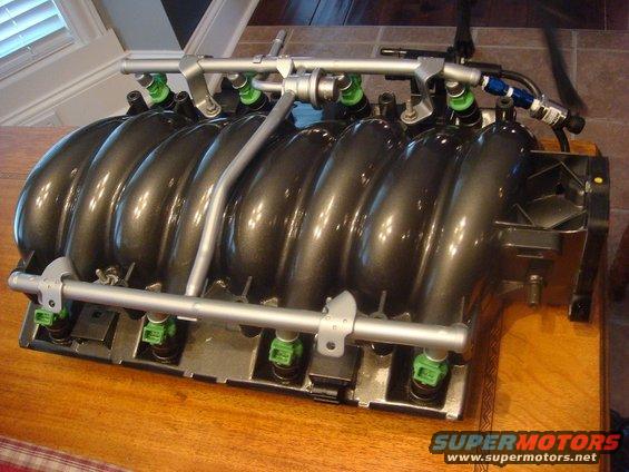 Dark gray engine intake manifold with green fuel injectors and silver fuel rails