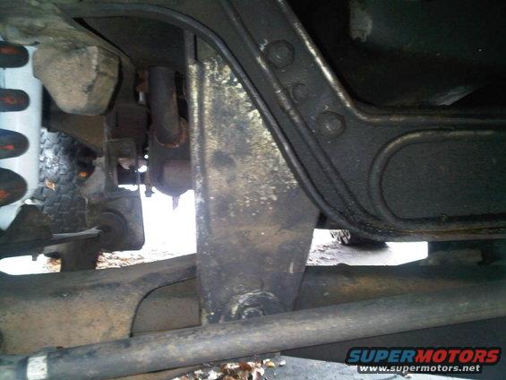 Undercarriage of a vehicle showing suspension components, exhaust pipe, and frame rails. The part is dirty and shows signs of wear