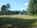 1989 Ford Bronco - A wide view of a rural property a house, a round hay bale in a mowed field, and surrounding trees on a sunny day.