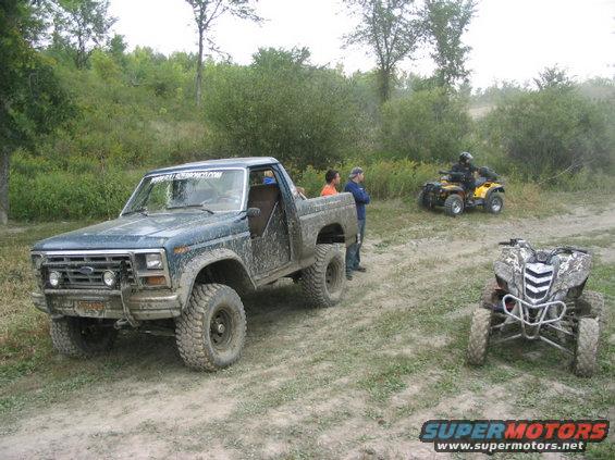 Mud-covered 1980 Ford F-Series pickup truck parked on dirt road with two ATVs nearby