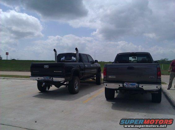 Rear view of two pickup trucks, one black with large exhaust pipes, one dark gray