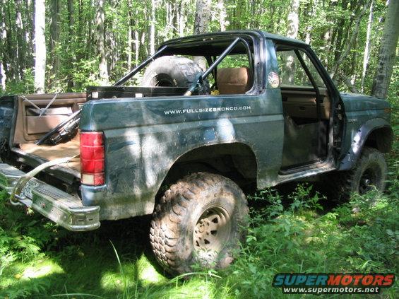 Green Ford Bronco with roll cage and spare tire in back, parked in woods