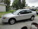 2003 Ford Taurus - A silver 2003 Ford Taurus sedan is parked on a concrete driveway, with the front passenger side elevated by a blue jack.