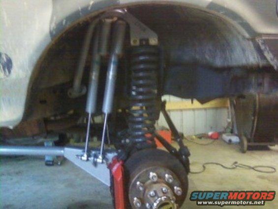 Close-up of a vehicle's front suspension with dual shocks, large coil spring, and red brake caliper